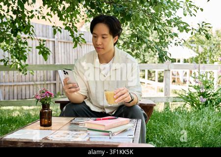Freelancer relaxes outdoors with a drink while using his phone on a sunny day Stock Photo