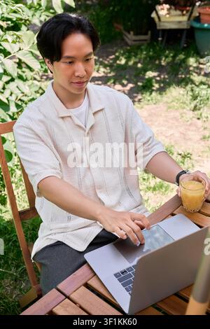 Freelancer enjoys remote work outdoors while sipping a refreshing drink in summer Stock Photo