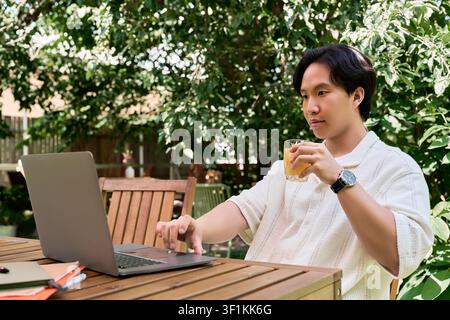 Freelancer enjoys remote work at a sunny terrace cafe surrounded by greenery Stock Photo