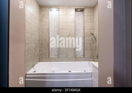 Modern bathroom with a white jacuzzi tub surrounded by tan tiles and decorative tiled niches Stock Photo