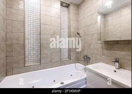clean bathroom featuring a white bathtub, tiled walls in neutral tones with mosaic accents, a sink with a vanity, and a mirror Stock Photo