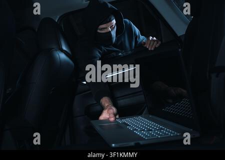 Car items theft - robber steals laptop from car interior through window Stock Photo