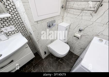 bathroom featuring a white toilet, sink, washing machine, and mixed marble tiles Stock Photo