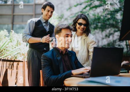 Business colleagues having an outdoor meeting around a laptop, smiling and collaborating Stock Photo