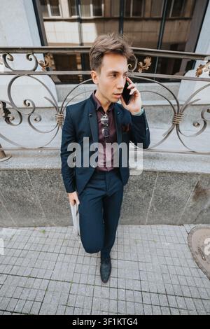 Young businessman talking on phone outside by city railing holding a newspaper Stock Photo