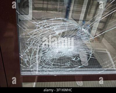 Glass in a window shows damage with cracks in a circular pattern during daylight outside a building in an urban area Stock Photo