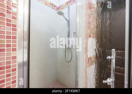 shower stall with mosaic tiles, a shower head, and a glass door Stock Photo