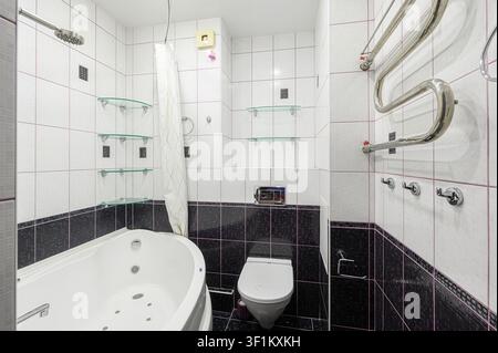 bathroom featuring a white bathtub with jets, a toilet, and tiled walls with glass shelves Stock Photo