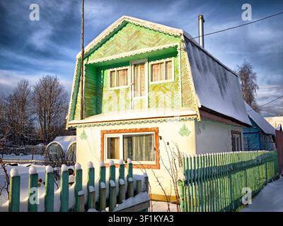 Wooden houses stand in a snowy rural village in Russia. Fences and roofs are covered with snow, showing village life during winter. Stock Photo