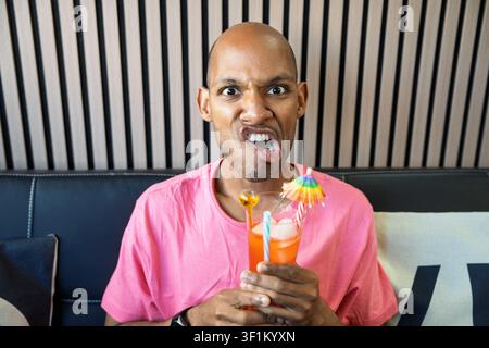Young man making a silly face, holding a colorful drink with a small umbrella, expressing humor and joy Stock Photo