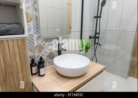 Modern bathroom with a round white sink, black faucet, geometric tile backsplash, and a shower with black fixtures Stock Photo
