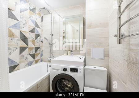 compact bathroom with patterned tile, a washing machine under the sink, and a toilet close by. Bright and functional Stock Photo