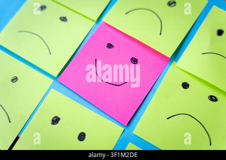 smiling face among sad and angry faces drawing on sticky papers, concept of positivity and happines attitude in a sad world Stock Photo