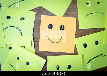 smiling face among sad and angry faces drawing on sticky papers, concept of positivity and happines attitude in a sad world Stock Photo