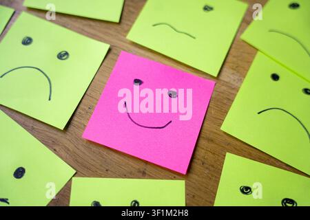 smiling face among sad and angry faces drawing on sticky papers, concept of positivity and happines attitude in a sad world Stock Photo