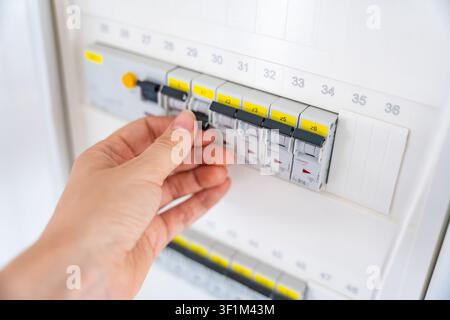 Hand switching an electrical circuit breaker in a residential distribution panel. Electrical safety and power control support maintenance, energy Stock Photo