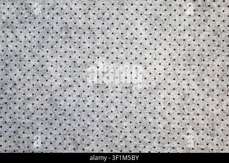 A macro, full-frame shot showcasing the detailed texture of a grey perforated nonwoven felt fabric, featuring a clean, geometric grid pattern of black Stock Photo