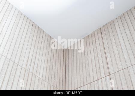 A close-up, low-angle shot of a room corner showing light beige, vertically ribbed wood-effect ceramic tiles on two adjacent walls meeting a plain, sm Stock Photo