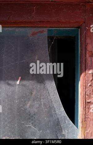Vertical close up of a broken dirty glass in an old wooden window frame with peeling red paint Stock Photo