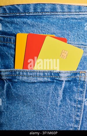 Close-up of three multicolored microchip credit cards protruding from the back pocket of a pair of jeans. E-commerce payment security concept. Persona Stock Photo