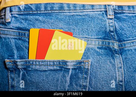 Close-up of three multicolored microchip credit cards protruding from the back pocket of a pair of jeans. E-commerce payment security concept. Persona Stock Photo