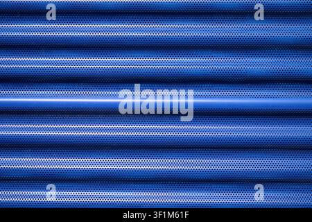 Background created with a close-up of a blue, striated, and perforated metallic surface from the facade of a modern building. Industrial panel manufac Stock Photo