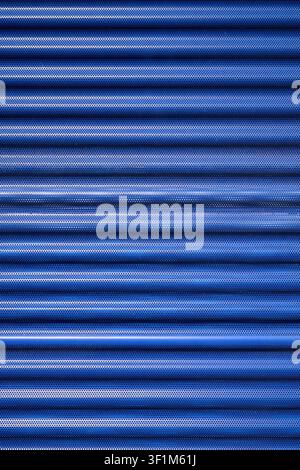 Background created with a close-up of a blue, striated, and perforated metallic surface from the facade of a modern building. Industrial panel manufac Stock Photo