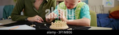 Child with Down Syndrome engaging in fine motor learning activity with caregiver guidance, supporting inclusive development. Useful for therapy, education, parenting campaigns, close up Stock Photo