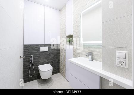 modern, minimalist bathroom with gray and white tones, featuring a floating toilet, sleek sink, and LED mirror Stock Photo