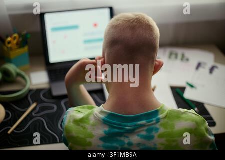 Rear view of child studying on laptop at desk, following online lesson and doing homework. Concept for remote learning, homeschooling, digital education marketing Stock Photo