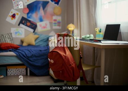 Wide shot of child bedroom showing backpack hanging on chair beside laptop desk, suggesting home study routine and school readiness. Ideal for education, back to school, parenting campaigns Stock Photo