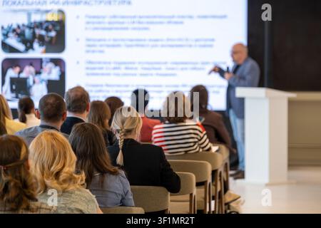 Group of professionals seated watching presenter using large screen, focused atmosphere, corporate training and networking. Stock Photo