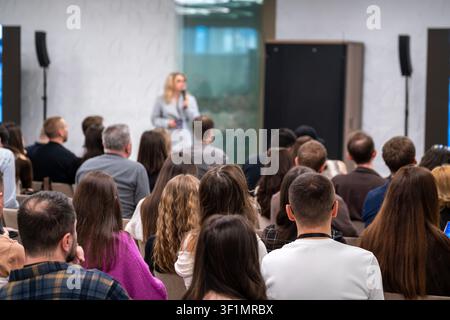 Audience listening to speaker during professional conference presentation, focused attendees, networking, learning, corporate training atmosphere. Stock Photo