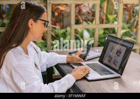 Young woman using laptop and phone while working outside in green environment Stock Photo