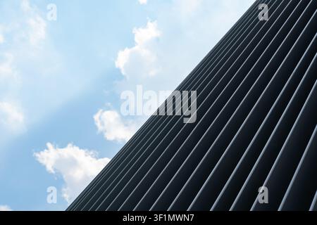 Low angle view of a modern building facade with repeating dark metal ribs, creating strong lines and geometric pattern, set against a bright blue sky Stock Photo