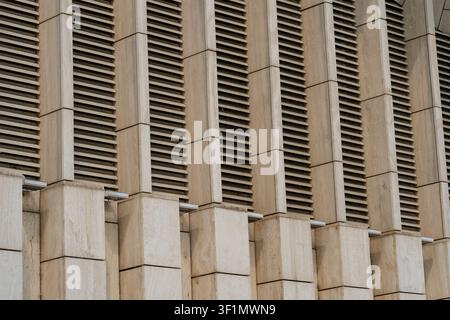 Close-up of a modern building facade showing repeating concrete columns and horizontal louvers, creating a geometric pattern, texture, and rhythmic ar Stock Photo