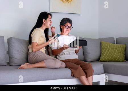 A loving moment between a Chinese mother and her daughter as they share quality time on the couch using digital devices, highlighting family bonds and Stock Photo