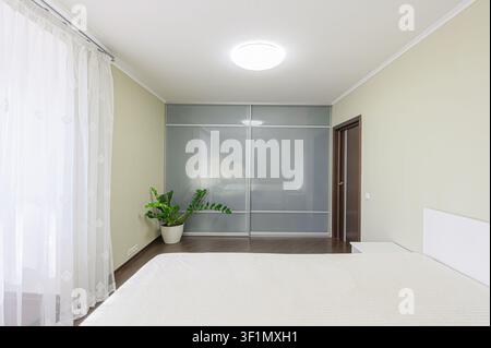 bright bedroom featuring a large bed, sliding door wardrobe, and neutral color palette. Simple, modern design Stock Photo