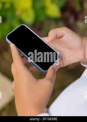 Hand holding smartphone with blank screen against green outdoor background Stock Photo