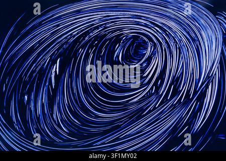 Abstract 3D render of glowing blue light trails spiraling into a vortex tunnel on dark background, evoking speed, data flow, cyberspace, and futuristi Stock Photo