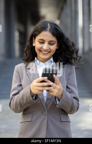 Happy professional woman in a suit using a mobile phone to communicate, text, and connect with technology while standing in an urban environment Stock Photo