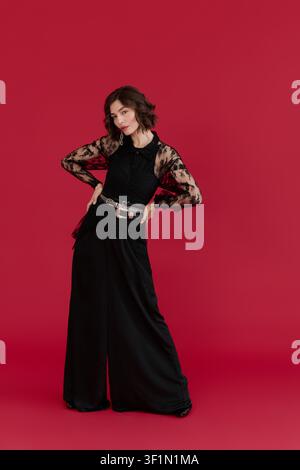 Young woman showcases elegance in a black lace blouse within a striking red backdrop Stock Photo