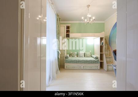 charming children's room with a bunk bed, mint green walls, and cream-colored furniture. Soft lighting and airy curtains create a cozy atmosphere Stock Photo