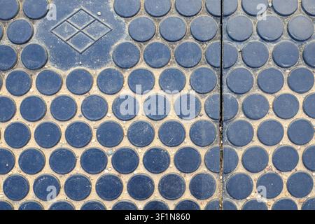 Anti-slip rubber panels on a pedestrian railway crossing. Textured black safety pavement surface with a pattern of circular bumps, diamond logo and sa Stock Photo