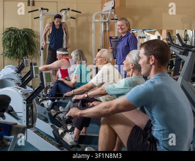 Group of people using rowing machine with instructor at gym Stock Photo
