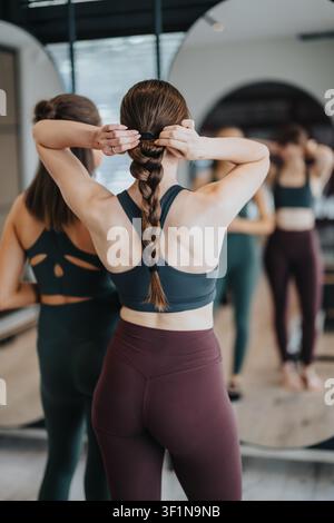 Woman in active wear tying braided hair in front of mirror at a fitness studio workout Stock Photo