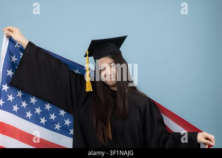Happy graduate female student holding american flag behind her back in the st... Stock Photo