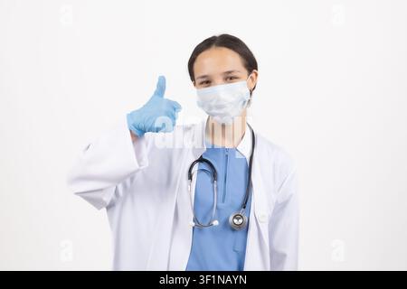 Happy female doctor wearing protective face mask showing thumbs up in the studio Stock Photo