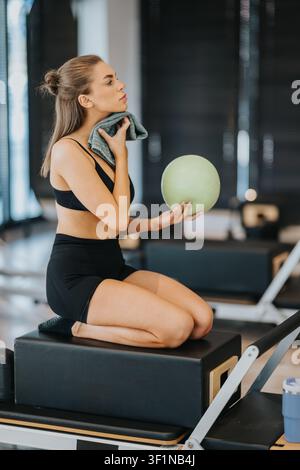 Fit woman doing pilates exercises with a small exercise ball on reformer box in studio Stock Photo
