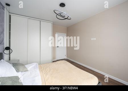 bedroom interior with neutral tones, featuring a bed, wardrobe, and modern lighting Stock Photo